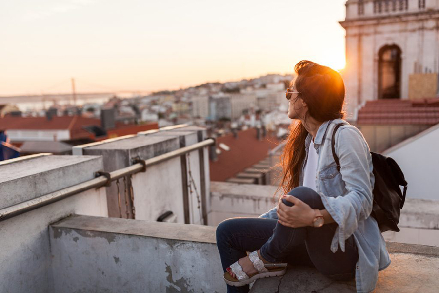 Frau sitzt auf einer alten Mauer und genießt die Aussicht über die Altstadt im Sonnenuntergang.