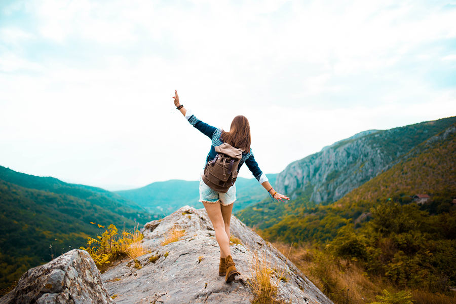EIne junge Frau in kurzer Hose mit Rucksack wandert auf einer Klippe in den Bergen und genießt die Natur, Ihren Urlaub in den Bergen.