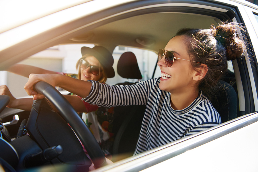 Zwei attraktive junge Frauen mit Sonnenbrillen fahren an einem sonnigen Tag mit dem Auto durch die Stadt und reden und lachen dabei