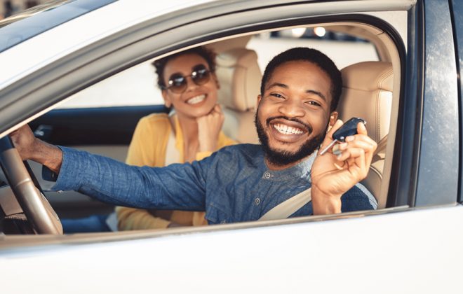 Ein lächelndes afroamerikanisches Pärchen, das im Auto sitzt. Der Mann hält den Autoschlüssel hoch.