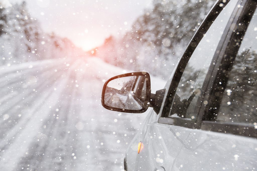 Blick auf den linken Seitenspiegel eines Autos, das eine schneebedeckte Straße befährt