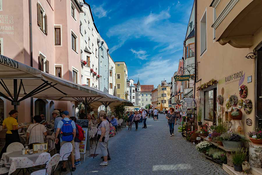Blick auf belebte Straße in einer Altstadt, die von Restaraunts und einem Blumenladen gesäumt ist