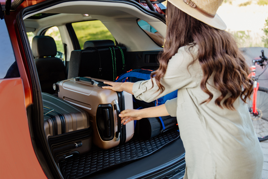 Frau mit braunen langen Haaren und Hut schiebt Koffer in einen Kofferraum