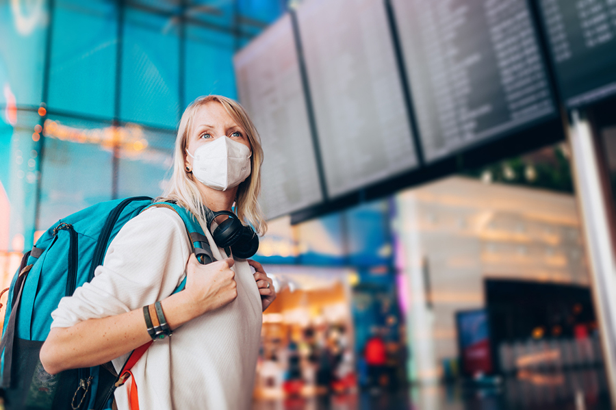 Frau mit Rucksack und Maske steht in der Halle eines Flughafens