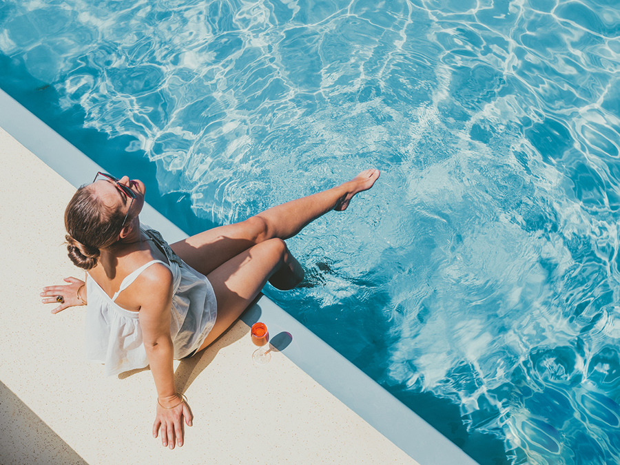 Frau sitzt am Rand eines Pools und hält Füße ins Wasser